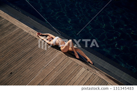 Top view, lying down. Woman in white bikini is near swimming pool 131345483