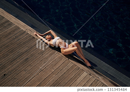 Top view, lying down. Woman in white bikini is near swimming pool 131345484