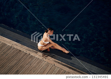 Resting, enjoying the vacation. Woman in white bikini is near swimming pool 131345491