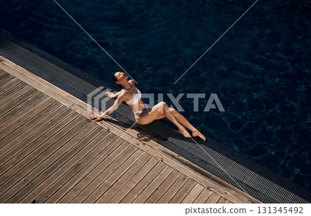Resting, enjoying the vacation. Woman in white bikini is near swimming pool 131345492