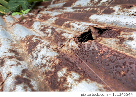 Close-up of rusty corrugated metal sheet with a hole, corrosion texture and decay detail 131345544