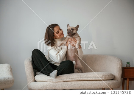 Front view, sitting on the little sofa. Young woman is with her pug dog at home 131345728