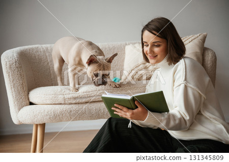 Reading the book. Young woman is with her pug dog at home Reading the book. Young woman is with her pug dog at home 131345809