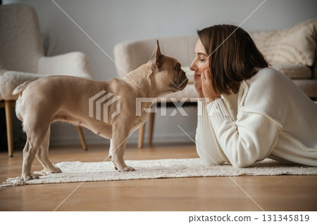 Looking at each other, lying down on floor. Young woman is with her pug dog at home Looking at each other, lying down on floor. Young woman is with her pug dog at home 131345819