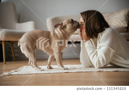 Looking at each other, lying down on floor. Young woman is with her pug dog at home Looking at each other, lying down on floor. Young woman is with her pug dog at home 131345820