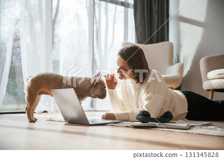 With laptop. On the floor. Young woman is with her pug dog at home 131345828