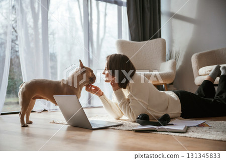With laptop. On the floor. Young woman is with her pug dog at home 131345833
