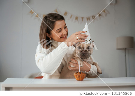 Happy birthday. Pet in hat and with cake. Young woman is with her pug dog at home Happy birthday. Pet in hat and with cake. Young woman is with her pug dog at home 131345866