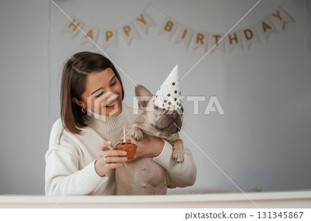 Happy birthday. Pet in hat and with cake. Young woman is with her pug dog at home Happy birthday. Pet in hat and with cake. Young woman is with her pug dog at home 131345867
