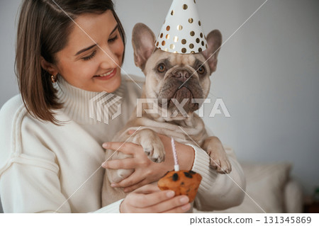 Celebration of birthday. In hats and with cake. Young woman is with her pug dog at home 131345869