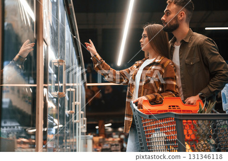 Side view, choosing products. Young couple are in supermarket together Side view, choosing products. Young couple are in supermarket together 131346118