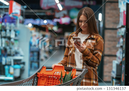 Using smartphone, standing. Woman is shopping in the supermarket 131346137