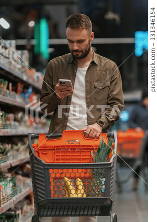Checking information in the phone. Man is shopping in the supermarket 131346154