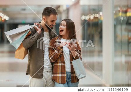 Excited people with smartphone. Young couple are in supermarket together Excited people with smartphone. Young couple are in supermarket together 131346199