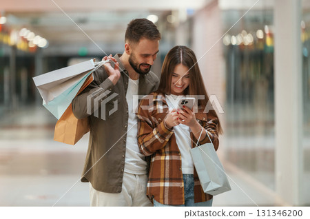 Excited people with smartphone. Young couple are in supermarket together Excited people with smartphone. Young couple are in supermarket together 131346200