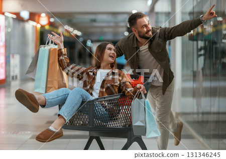 Fun in the mall, riding the shopping cart. Young couple are in supermarket together Fun in the mall, riding the shopping cart. Young couple are in supermarket together 131346245