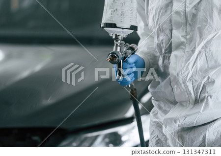 Focused close up view. Man is holding spray gun for painting a car 131347311