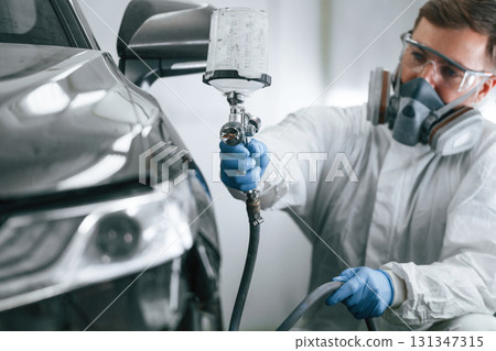 White protective wear. Man is painting a car by using spray guy 131347315