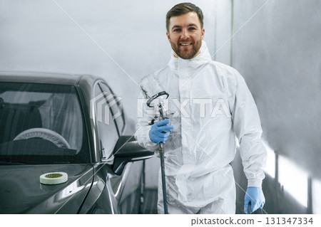 Bright artificial lighting. Man is standing and holding spray gun with paint for automobile 131347334
