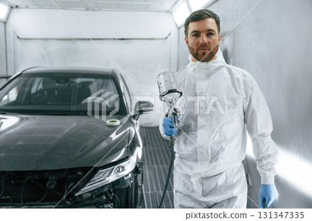 Bright artificial lighting. Man is standing and holding spray gun with paint for automobile 131347335