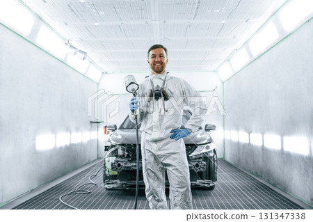 Bright artificial lighting. Man is standing and holding spray gun with paint for automobile 131347338