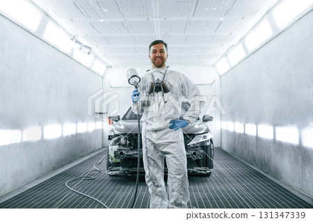 Man is standing and holding spray gun with paint for automobile 131347339
