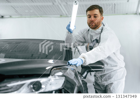 Front view. Garage worker is holding lighting and checking surface of the car 131347349