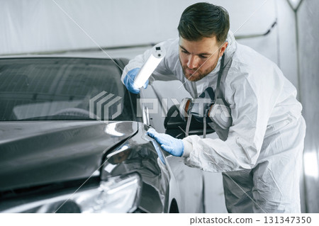 Front part of the automobile. Garage worker is holding lighting and checking surface of the car 131347350