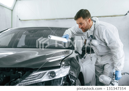 Front part of the automobile. Garage worker is holding lighting and checking surface of the car 131347354