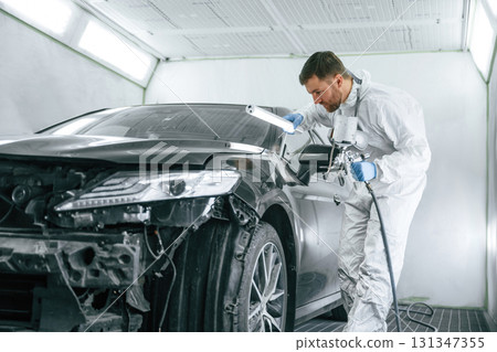 Professional worker. Man is painting a car by using spray guy 131347355