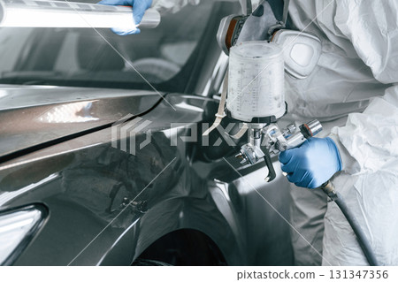 Professional worker. Man is painting a car by using spray guy Professional worker. Man is painting a car by using spray guy 131347356