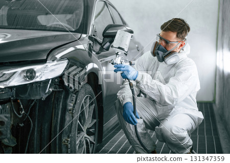 Professional worker. Man is painting a car by using spray guy 131347359