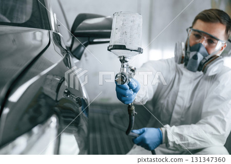 White protective wear. Man is painting a car by using spray guy 131347360