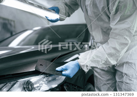Choosing right color. Garage worker is holding lighting and checking surface of the car 131347369