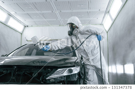 White protective wear. Man is painting a car by using spray guy 131347378