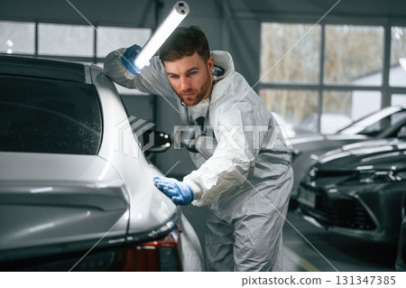 Rear part of automobile. Garage worker is holding lighting and checking surface of the car 131347385