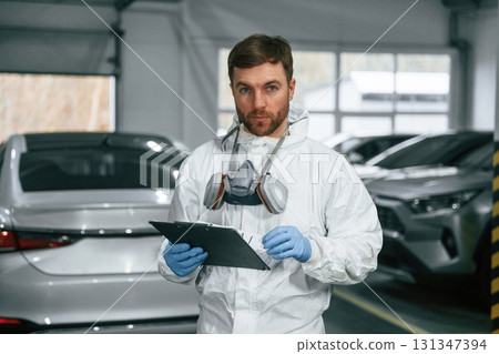 Portrait of car painter that is standing in the garage with documents in hands Portrait of car painter that is standing in the garage with documents in hands 131347394
