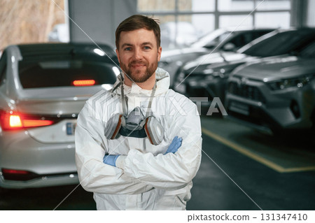 Standing in the garage with cars. Portrait of professional painter with mask 131347410