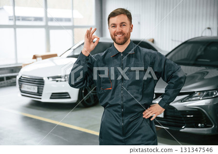 Handsome friendly guy. Repairman in uniform is standing in the garage with cars 131347546