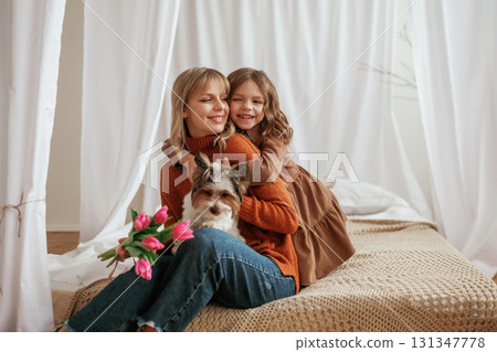 Holding flowers for mother's day holiday, embracing, with dog. Parent with daughter at home Holding flowers for mother's day holiday, embracing, with dog. Parent with daughter at home 131347778