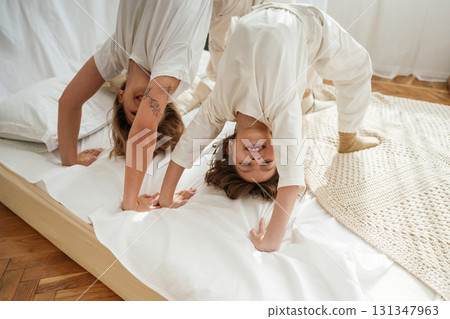 Playing in bed, standing on hands and legs. Mother with daughter are at home together Playing in bed, standing on hands and legs. Mother with daughter are at home together 131347963