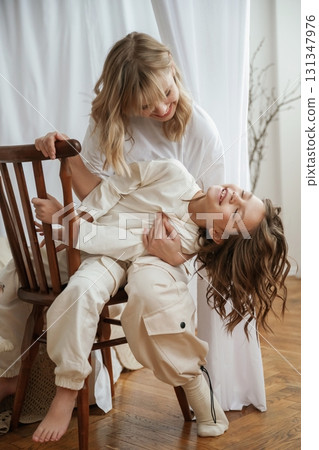 On the wooden chair. Mother with daughter are at home together On the wooden chair. Mother with daughter are at home together 131347976