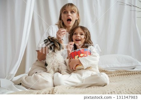 Watching movie with popcorn and dog. Mother with daughter are at home together Watching movie with popcorn and dog. Mother with daughter are at home together 131347983