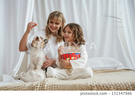 Feeding popcorn do a dog. Mother with daughter are at home together Feeding popcorn do a dog. Mother with daughter are at home together 131347986