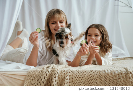 Cucumber beauty procedure. Cute dog. Mother with daughter are at home together Cucumber beauty procedure. Cute dog. Mother with daughter are at home together 131348013
