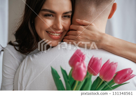 Woman is holding flowers and embracing the man. Young couple are together at home Woman is holding flowers and embracing the man. Young couple are together at home 131348561