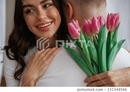 Close up view of woman holding flowers and hugs man. Young couple are together at home Close up view of woman holding flowers and hugs man. Young couple are together at home 131348566