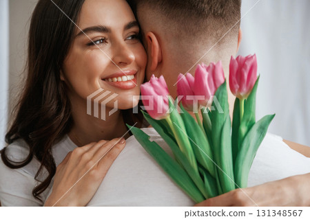 Close up view of woman holding flowers and hugs man. Young couple are together at home 131348567