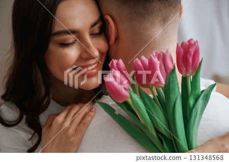 Happy woman with flowers embracing man. Young couple are together at home 131348568