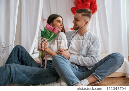Pink flowers in hands. Young couple are together at home Pink flowers in hands. Young couple are together at home 131348704